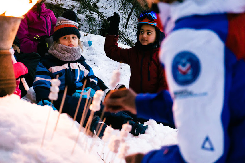 Enfants en combinaison de ski dans la neige avec des brochettes de chamallow